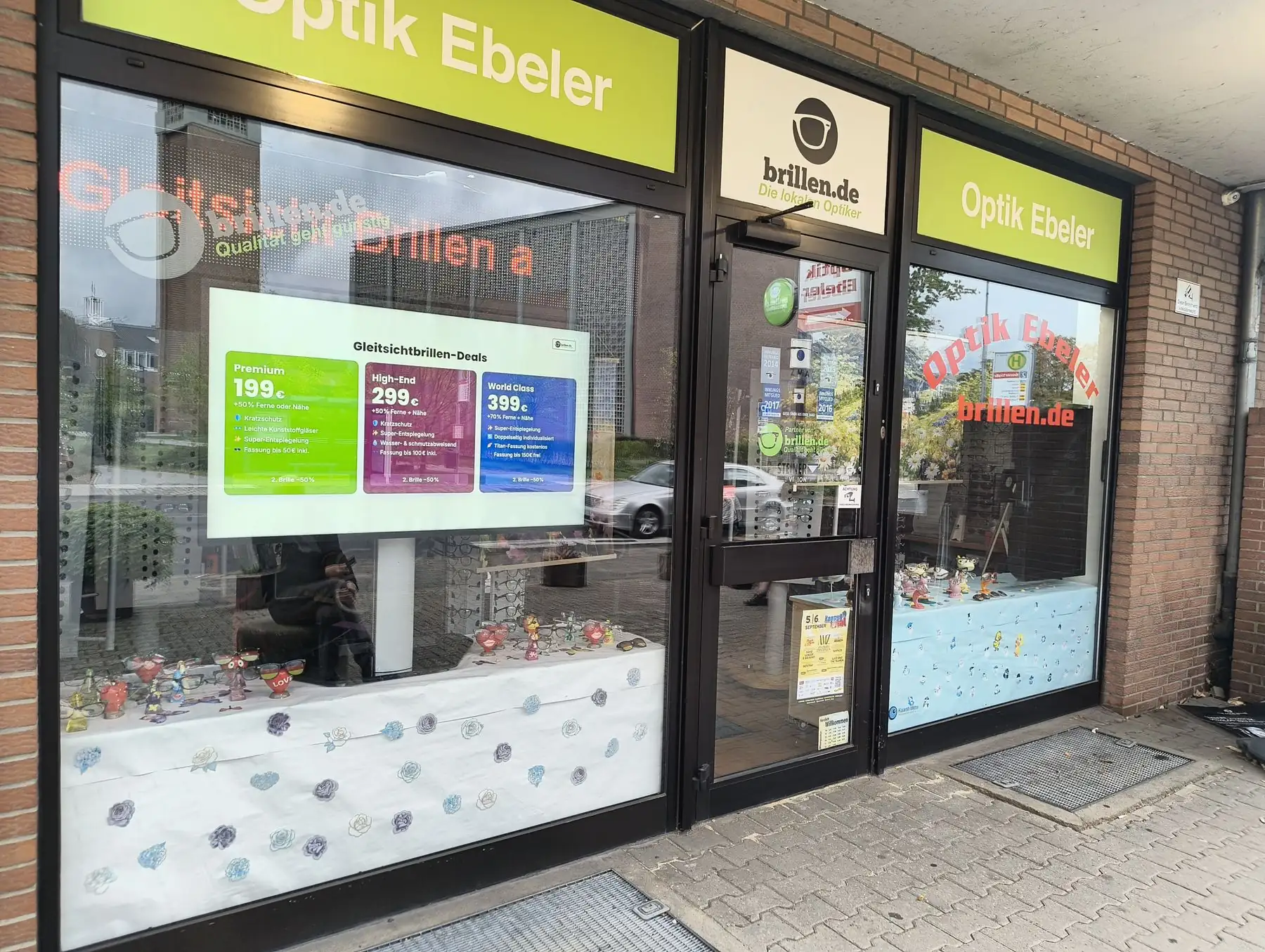 Blick von der Straße auf das Schaufenster von Optik Ebeler mit leuchtendem Display